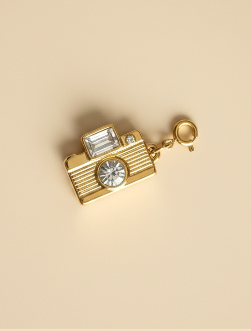 Gold camera-shaped charm with crystals on a beige background