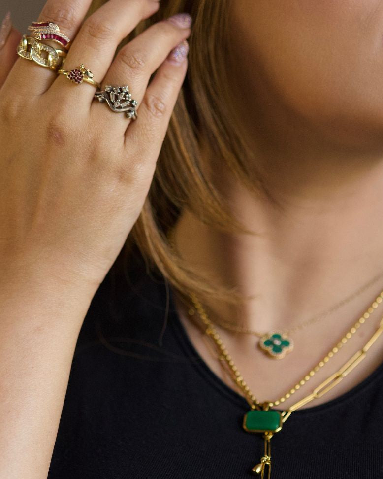 Close-up of a person wearing gold necklaces with green pendants.