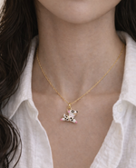Gold necklace with a small pendant worn by a person against a white shirt background