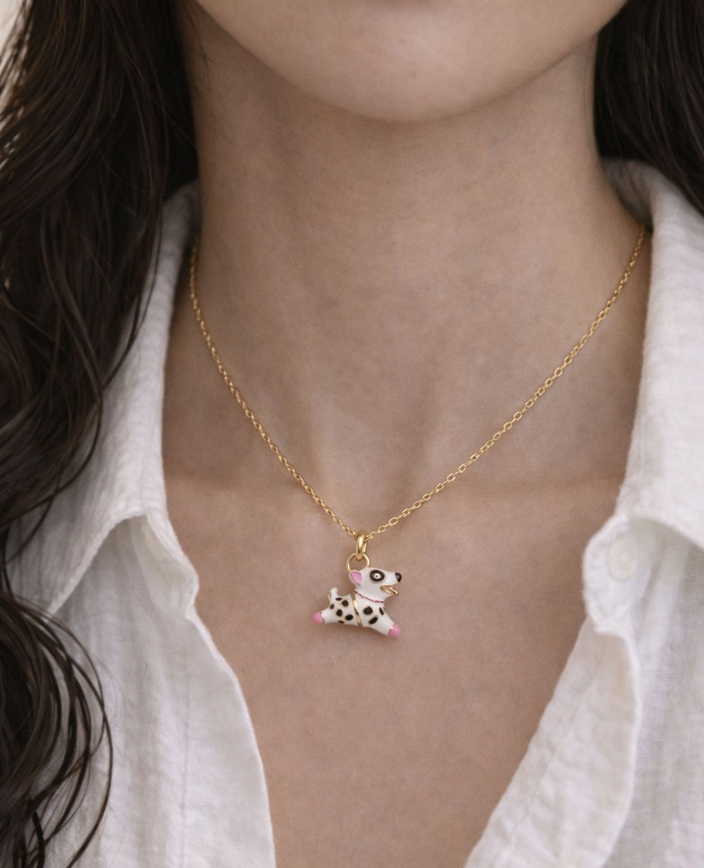 Gold necklace with a small pendant worn by a person against a white shirt background