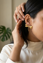Woman wearing gold dragonfly earrings with a neutral background