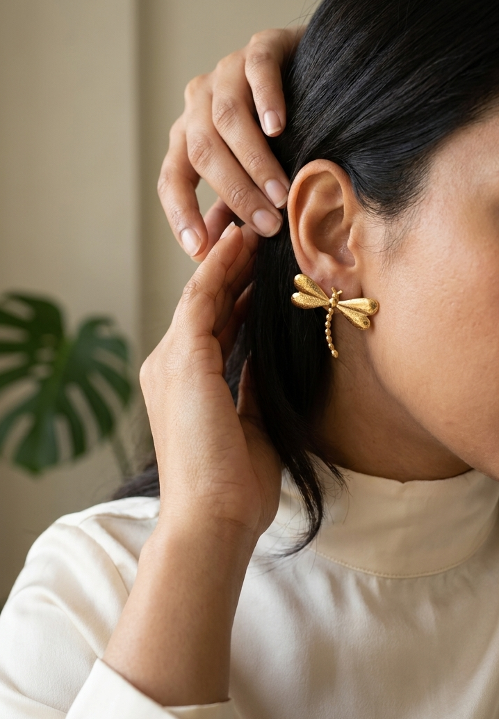 Woman wearing gold dragonfly earrings with a neutral background