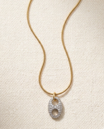 Gold necklace with a diamond pendant on a textured beige background