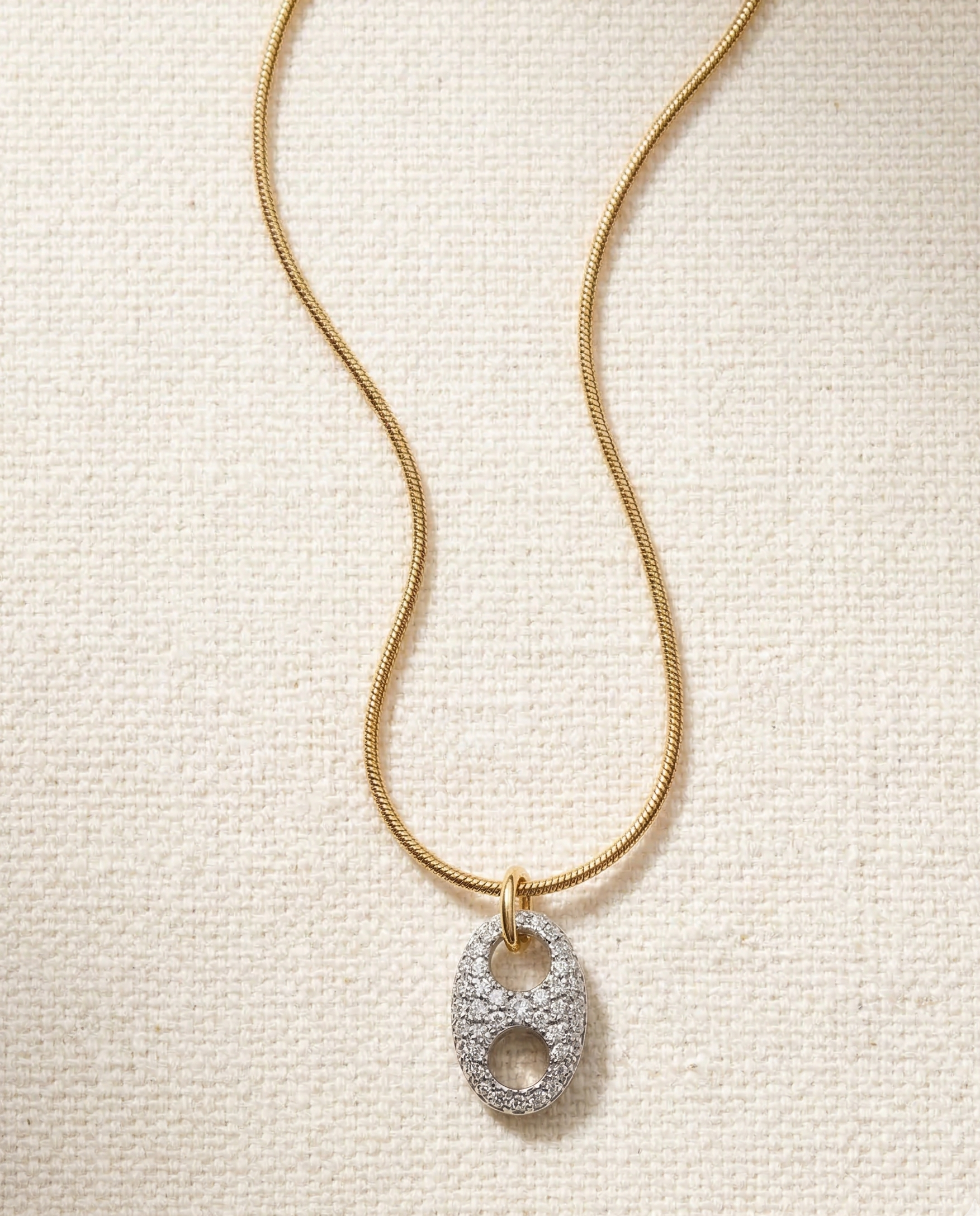 Gold necklace with a diamond pendant on a textured beige background