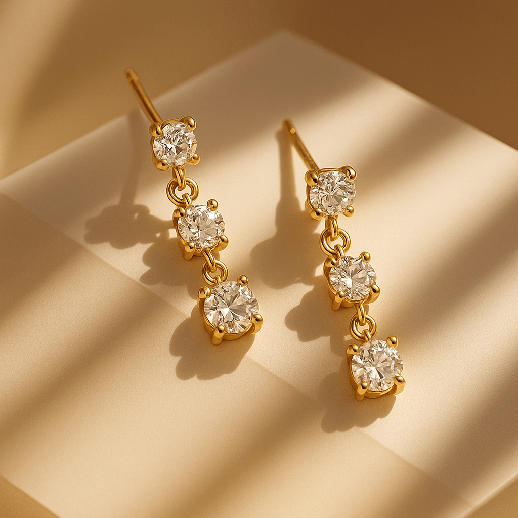 Gold earrings with clear gemstones on a beige surface