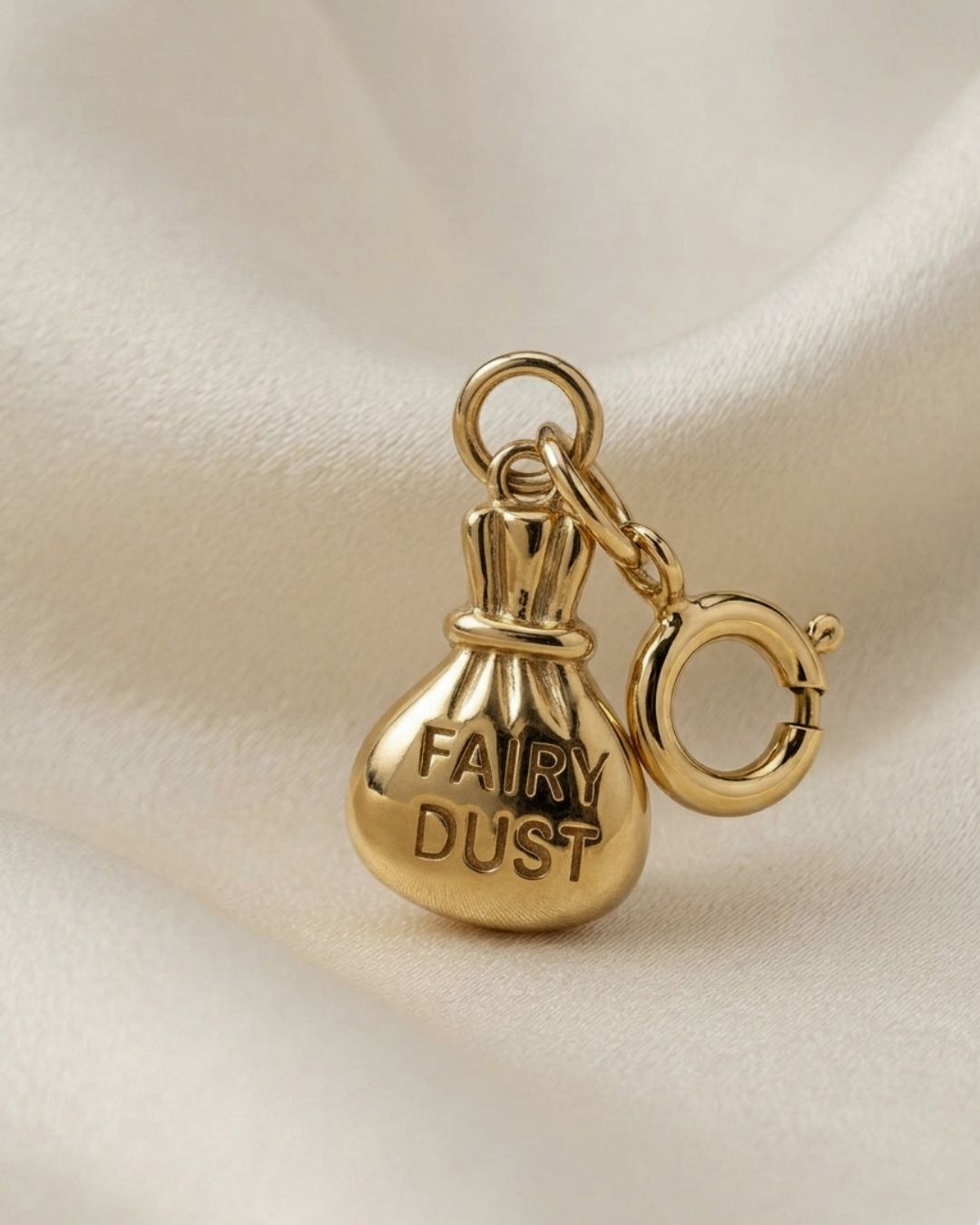 Gold 'Fairy Dust' charm on a beige fabric background