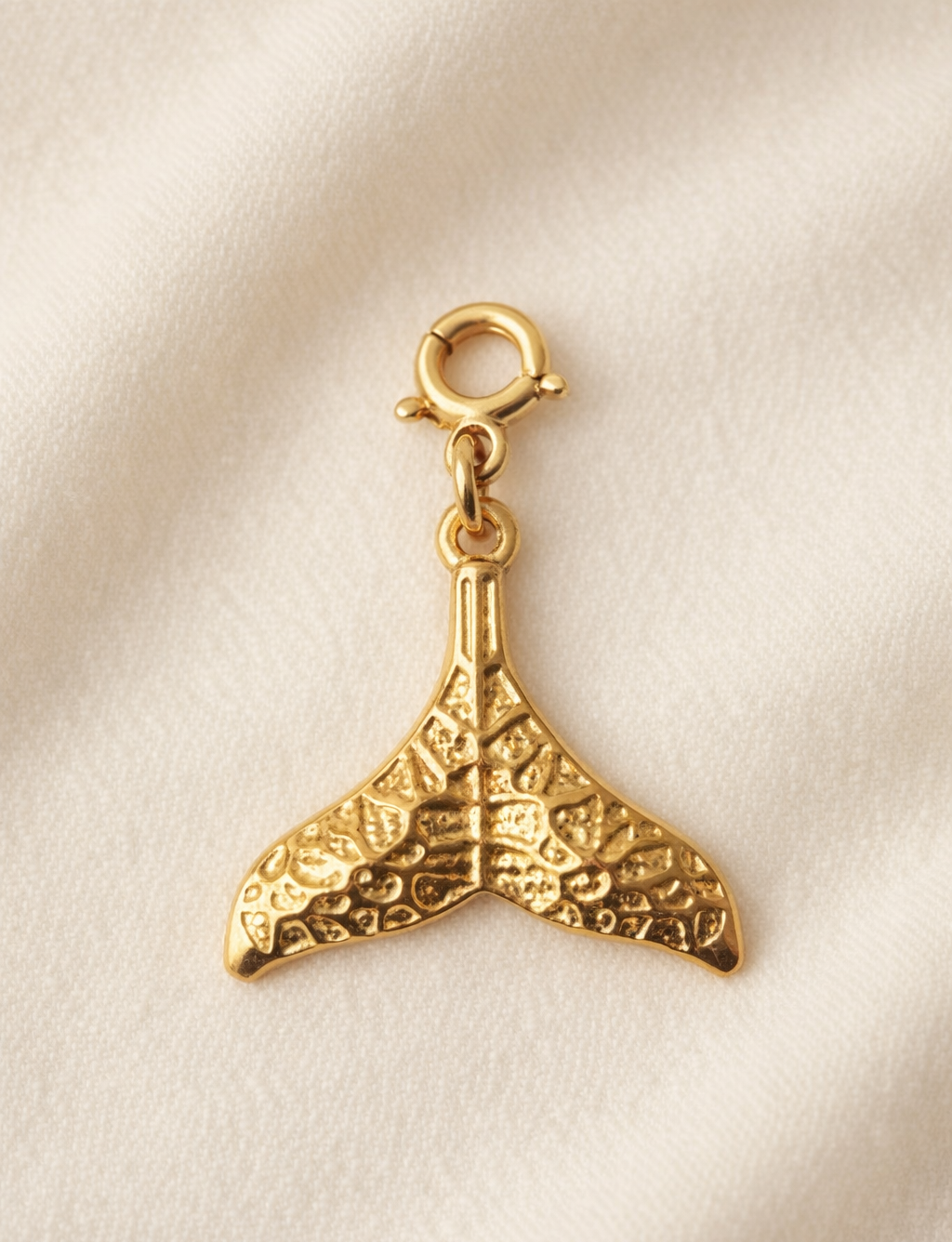 Gold whale tail charm on a beige background