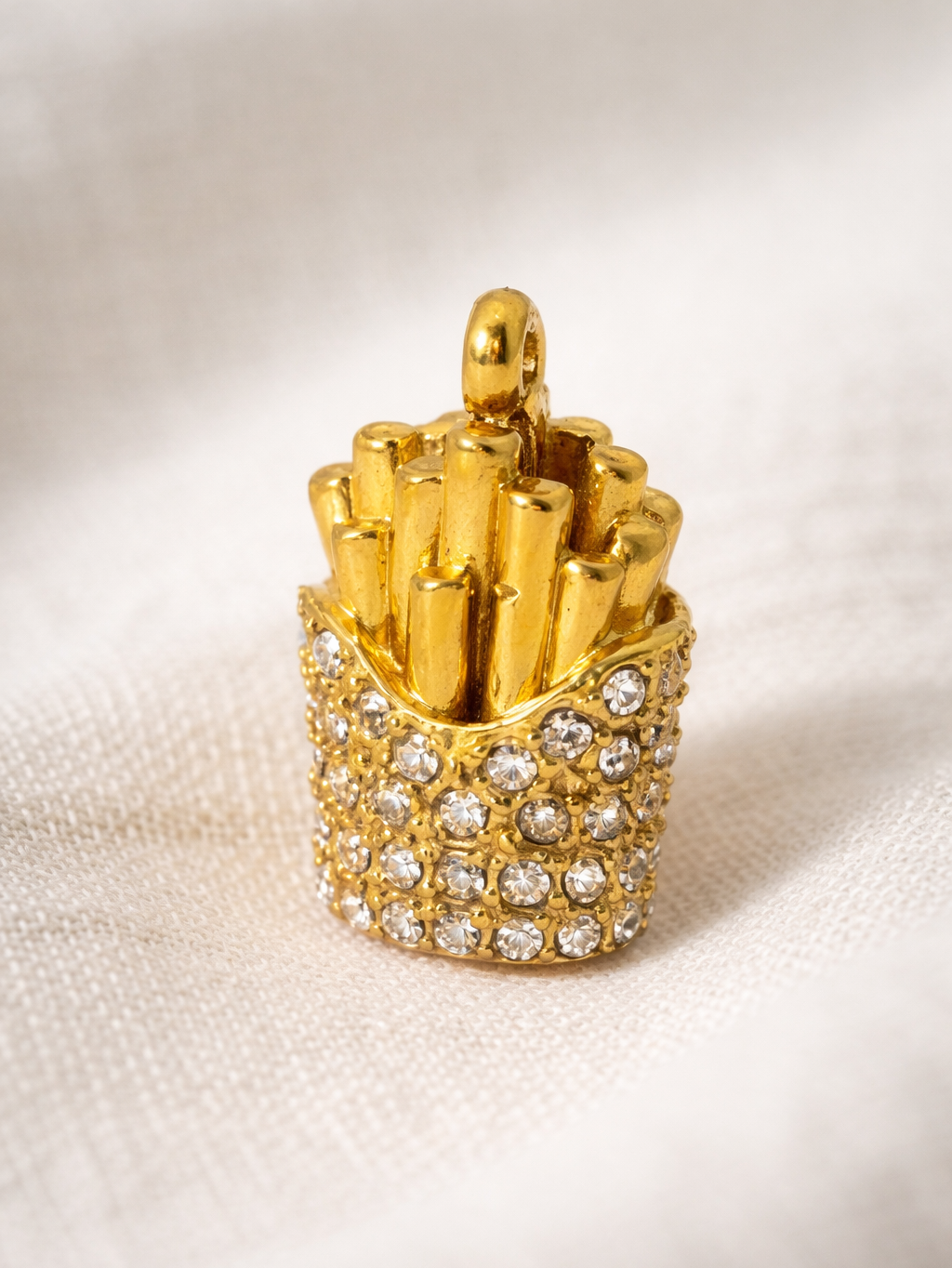 Gold French fry-shaped object with embedded crystals on a beige background
