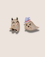 Two decorative pins, one with a devil face and the other with a bird face, on a beige background.