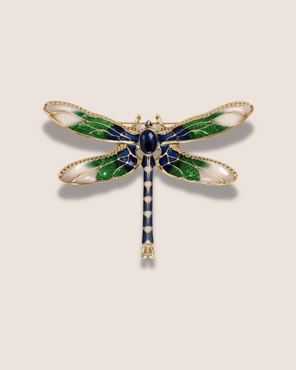 Dragonfly-shaped brooch with green, blue, and gold colors on a beige background