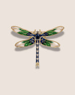 Dragonfly-shaped brooch with green, blue, and gold colors on a beige background