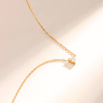 A delicate gold-tone heart-shaped necklace laid out on a plain surface, showcasing its elegant design and shiny finish.