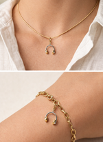 Gold necklace and bracelet with a unique headphone pendant on a neutral background