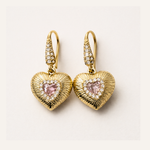 Gold heart-shaped earrings with pink gemstones on a light background