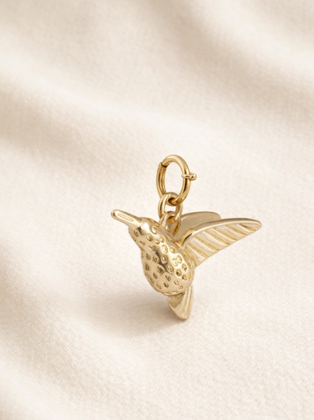 Gold hummingbird charm on a beige fabric background