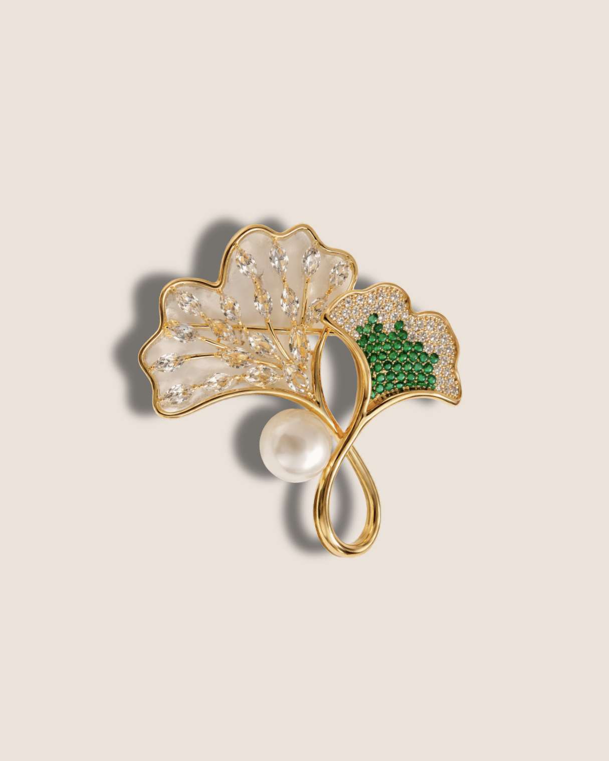 Gold leaf-shaped brooch with pearl and green gemstone on a beige background