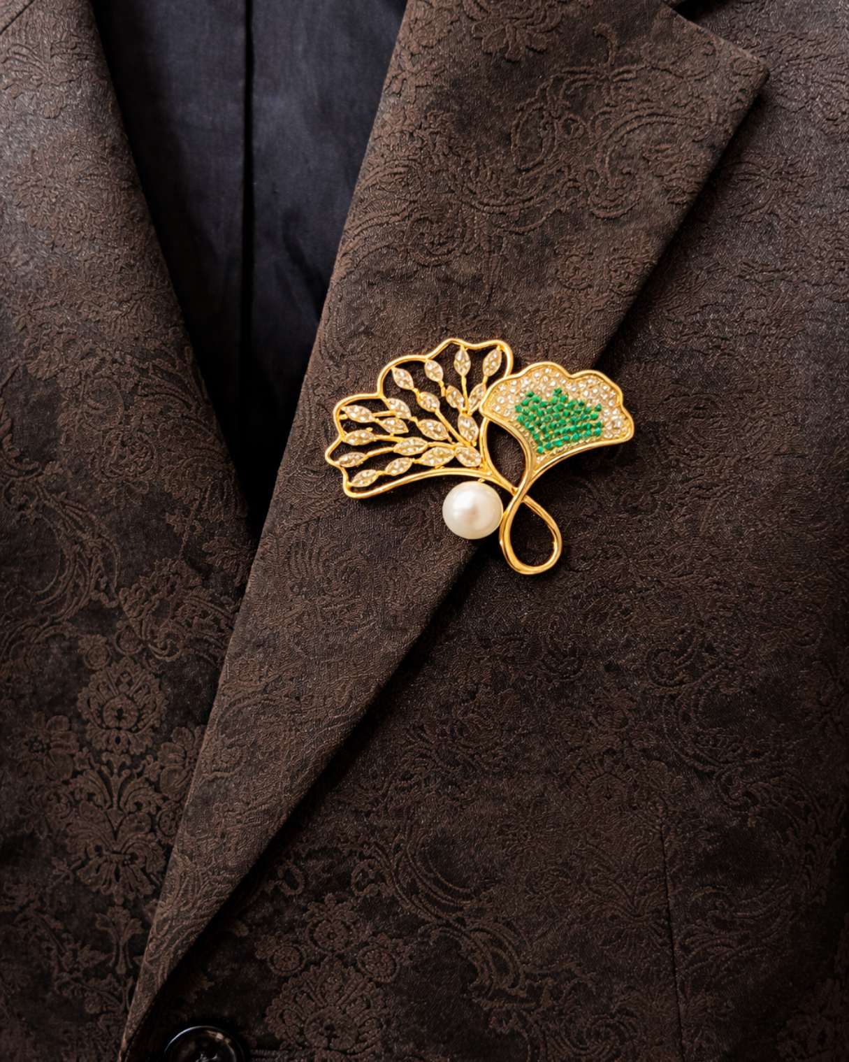 Gold brooch with green gem and pearl on a dark textured fabric background