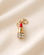 Lipstick-shaped charm with red lipstick and gold casing on a beige background