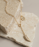 Gold necklace with leaf-shaped pendant on a stone surface