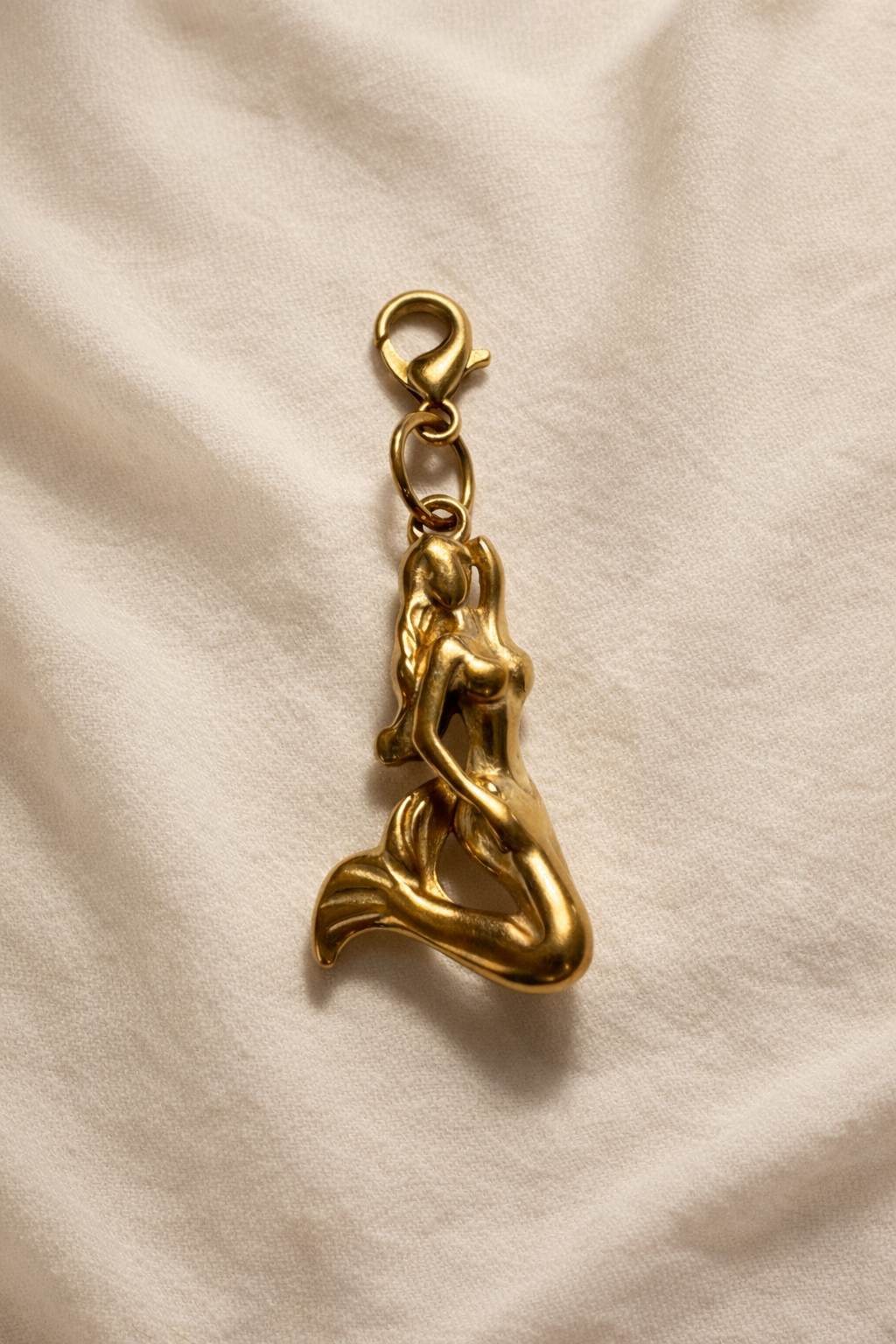 Gold mermaid charm on a beige fabric background