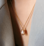 Gold necklace with a pearl pendant worn by a person against a neutral background