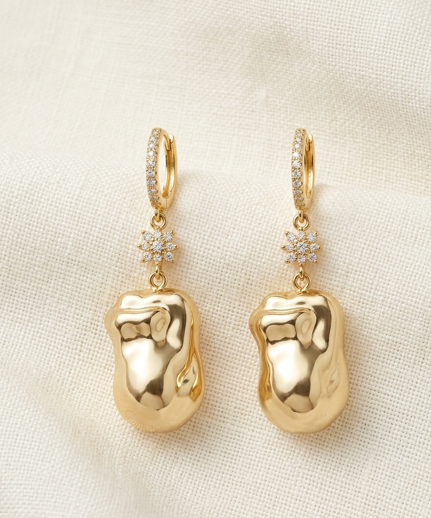 Gold baby footprint earrings with diamond accents on a beige fabric background