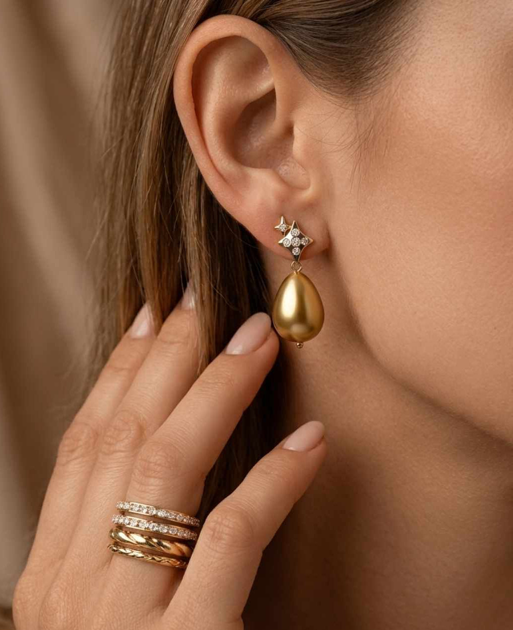 Gold teardrop earring with diamond accents worn by a person, against a neutral background.