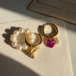 Gold hoop earrings with pearl and pink heart charms on a light surface