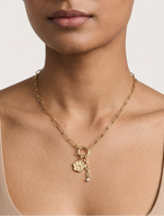 Woman wearing a gold necklace with a paw charm on a plain background