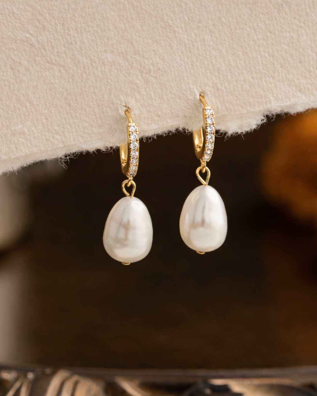 Pearl earrings with gold hoop and diamond accents on a textured beige surface