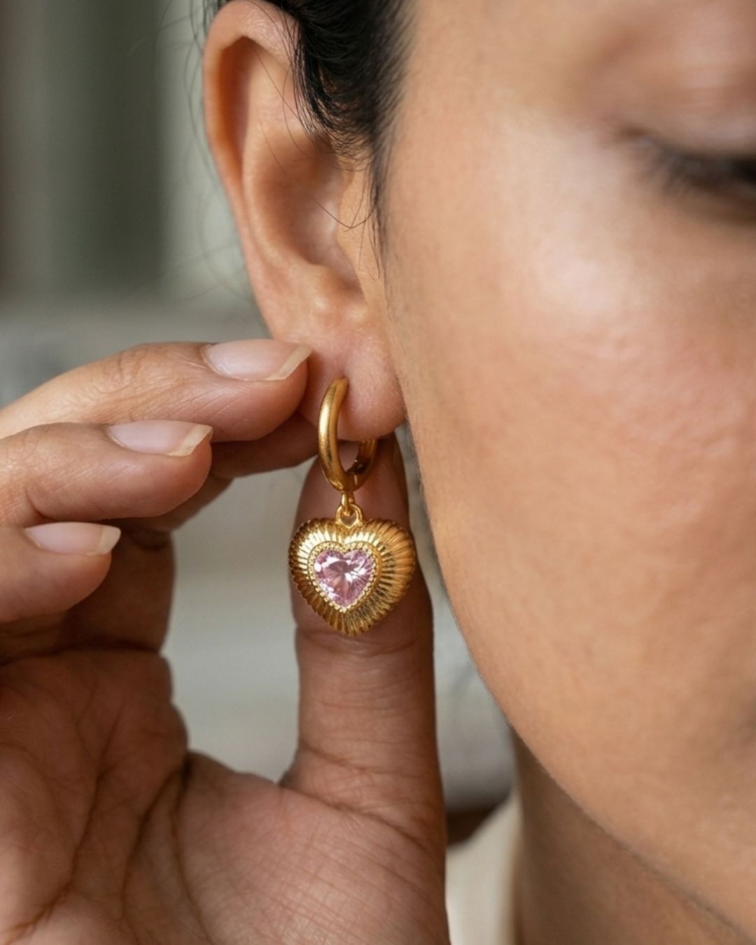 Close-up of a person wearing a gold heart-shaped earring with a pink gemstone.