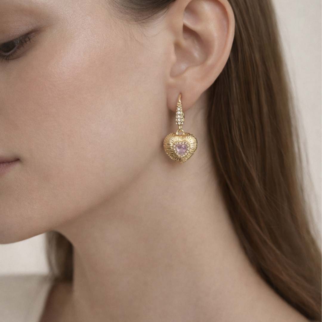 Gold heart-shaped earring with a pink gemstone worn by a model.