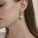 Gold heart-shaped earring with a pink gemstone worn by a model.