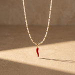 Pearl necklace with a red chili pepper pendant on a beige background