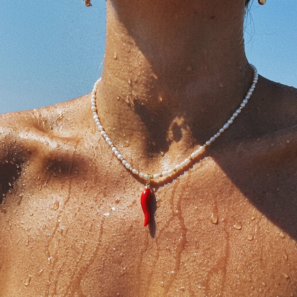 Close-up of a person wearing a pearl necklace with a red pendant against a blue sky.