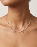 Necklace with small pendants on a person's neck against a neutral background
