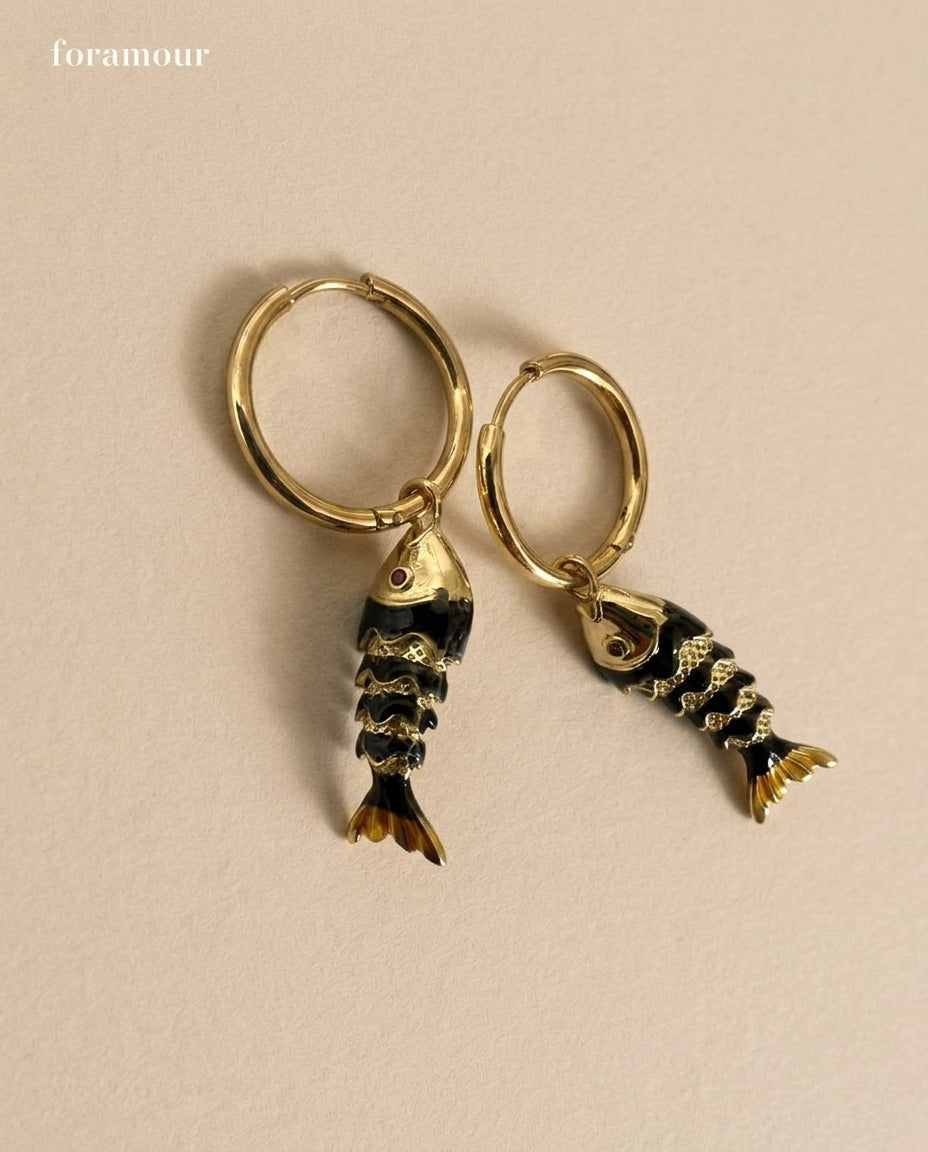 Gold hoop earrings with fish-shaped charms on a beige background
