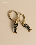 Gold hoop earrings with fish-shaped charms on a beige background