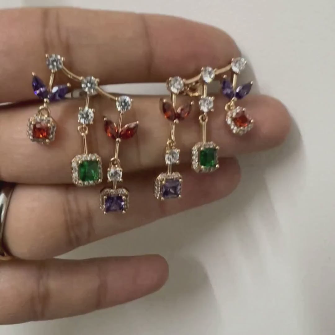 Long gold drop earrings with purple, red, emerald and amethyst halo stones stacked vertically on white surface
