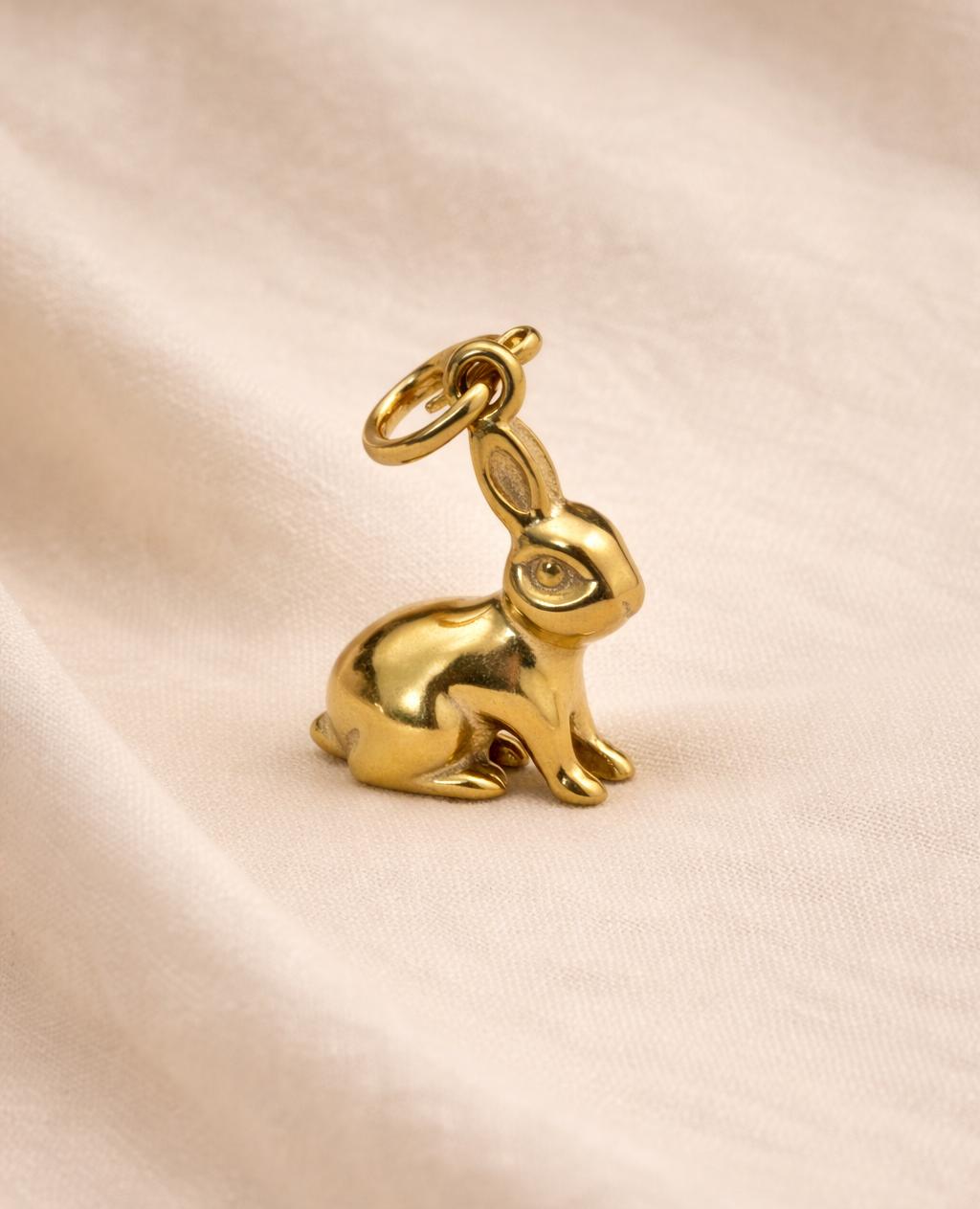 Gold rabbit charm on a beige fabric background