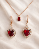 Rose gold jewelry set with red heart-shaped gemstones on a beige fabric background