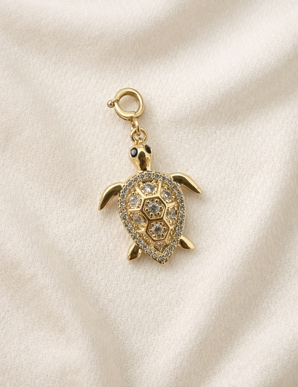 Gold turtle charm with gemstones on a beige fabric background