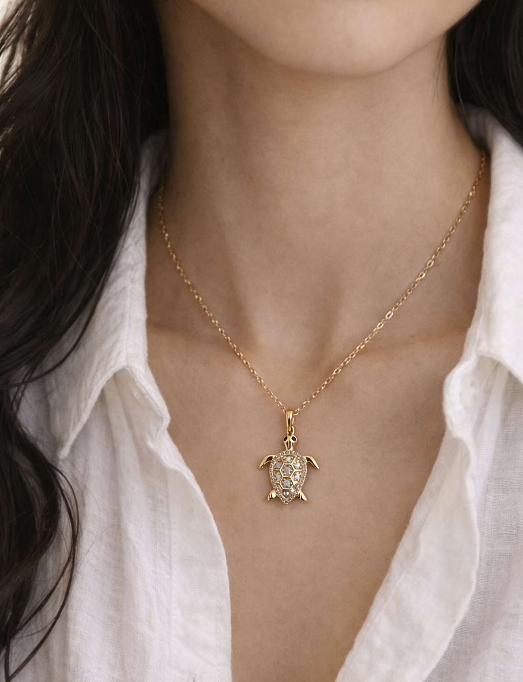 Gold turtle pendant necklace on a person wearing a white shirt