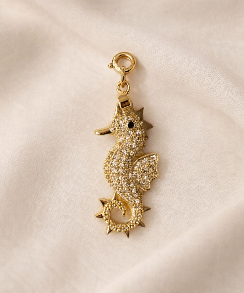 Gold seahorse-shaped charm on a beige fabric background