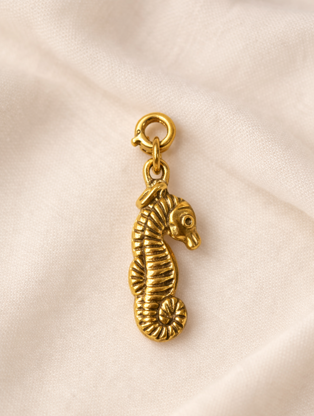 Gold seahorse charm on a beige fabric background