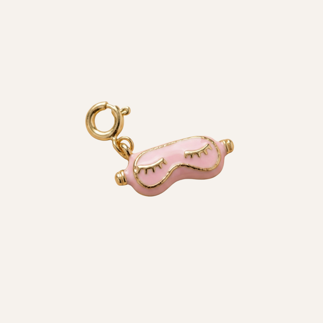 Pink eye mask charm with gold accents on a white background