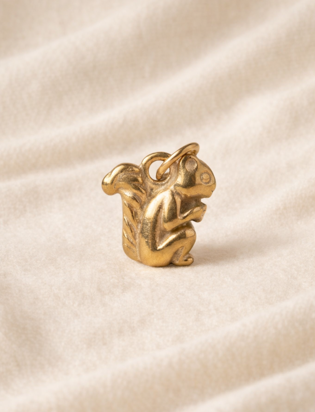 Gold charm shaped like a squirrel animal on a beige fabric background