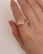 Gold ring with star design on a hand against a plain background