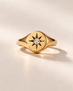 Gold ring with star design and diamond on a beige background