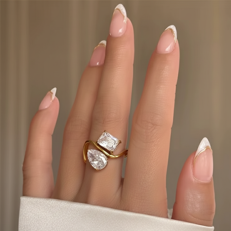 Gold ring with two large gemstones on a hand against a neutral background